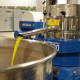 Frantoio oleario industriale durante il processo di estrazione dell’olio extravergine di oliva, con macchinari in acciaio inox e flusso di olio in uscita in primo piano.