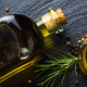 Bottiglia e ciotola di olio extravergine d'oliva su sfondo scuro, accompagnate da rametti di rosmarino e grani di pepe.
