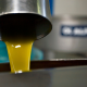 Flusso di olio extravergine di oliva appena spremuto che esce da un beccuccio in acciaio inox durante la fase di lavorazione in un frantoio locale.