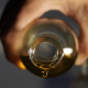 Primo piano di una mano che versa dell'olio extravergine di oliva da una bottiglia di vetro, con una goccia che sta per cadere.