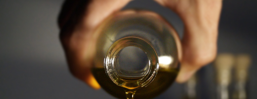 Primo piano di una mano che versa dell'olio extravergine di oliva da una bottiglia di vetro, con una goccia che sta per cadere.