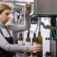 Donna che lavora in un frantoio imbottigliando olio extravergine di oliva in bottiglie di vetro scuro tramite una macchina automatica per l’imbottigliamento.