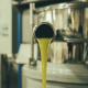 Macchinario per l’estrazione a freddo continua di olio extravergine di oliva, con il liquido verde che fuoriesce dal tubo in acciaio durante il processo di lavorazione artigianale.