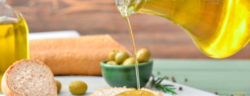 Olio extravergine di oliva versato su una fetta di pane, con olive verdi sullo sfondo, simbolo di qualità artigianale e tracciabilità nella filiera certificata.