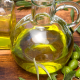 Bottiglie di vetro con olio extravergine di oliva su tavolo in legno, circondate da rami e frutti di ulivo verdi.