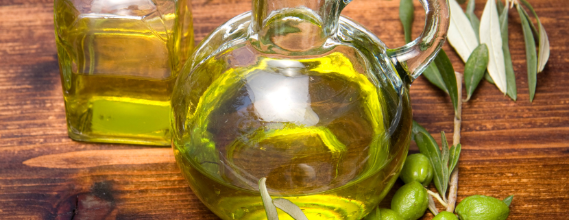 Bottiglie di vetro con olio extravergine di oliva su tavolo in legno, circondate da rami e frutti di ulivo verdi.