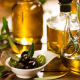Bottiglie e caraffa di olio extravergine di oliva su tavolo in legno, con ciotola di olive fresche e rami di ulivo decorativi.