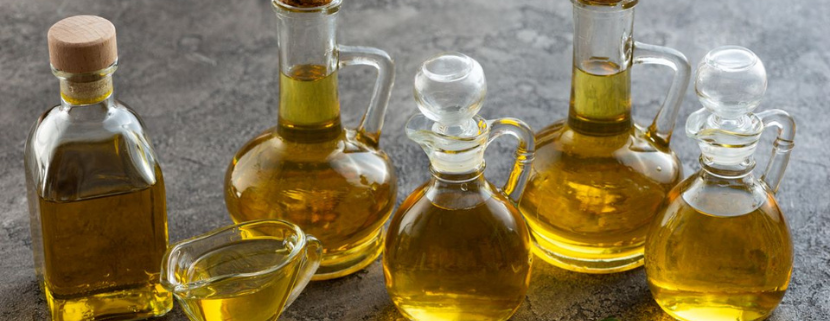Bottiglie e oliere di vetro piene di olio d’oliva disposte su un tavolo, con alcune olive verdi in primo piano, simbolo della produzione e classificazione dell’olio di oliva.