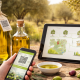 Bottiglie di olio extravergine d’oliva su un tavolo all’aperto con smartphone e tablet che mostrano QR code e tracciabilità della filiera produttiva dell’olio.